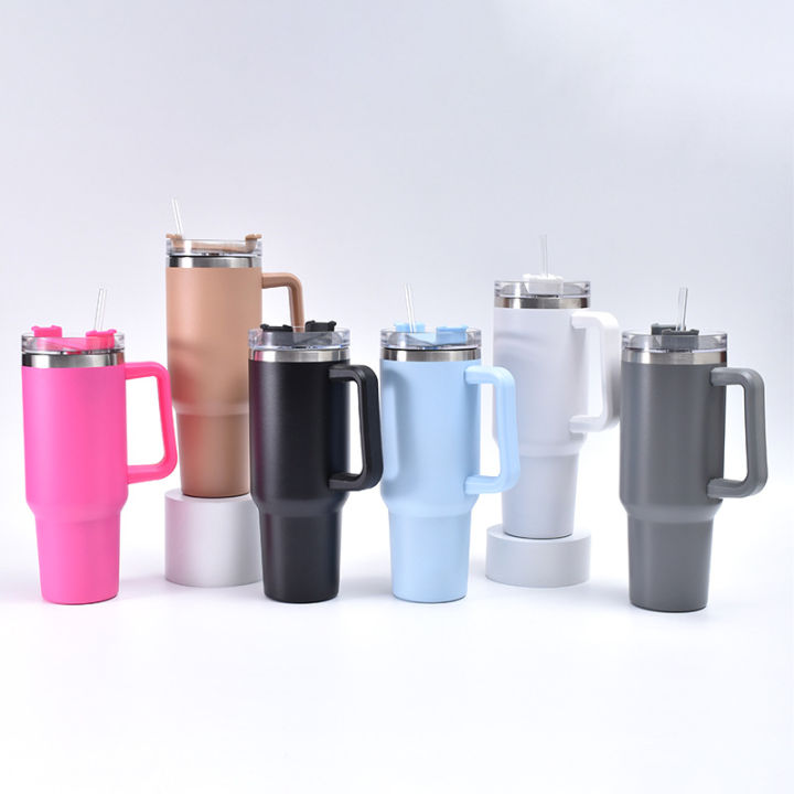 Collection of colorful insulated travel mugs on a desk with books and a laptop.