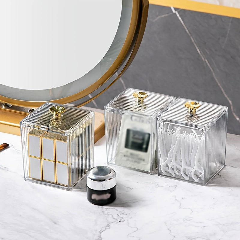 Two clear square containers with gold accents on a marble surface.